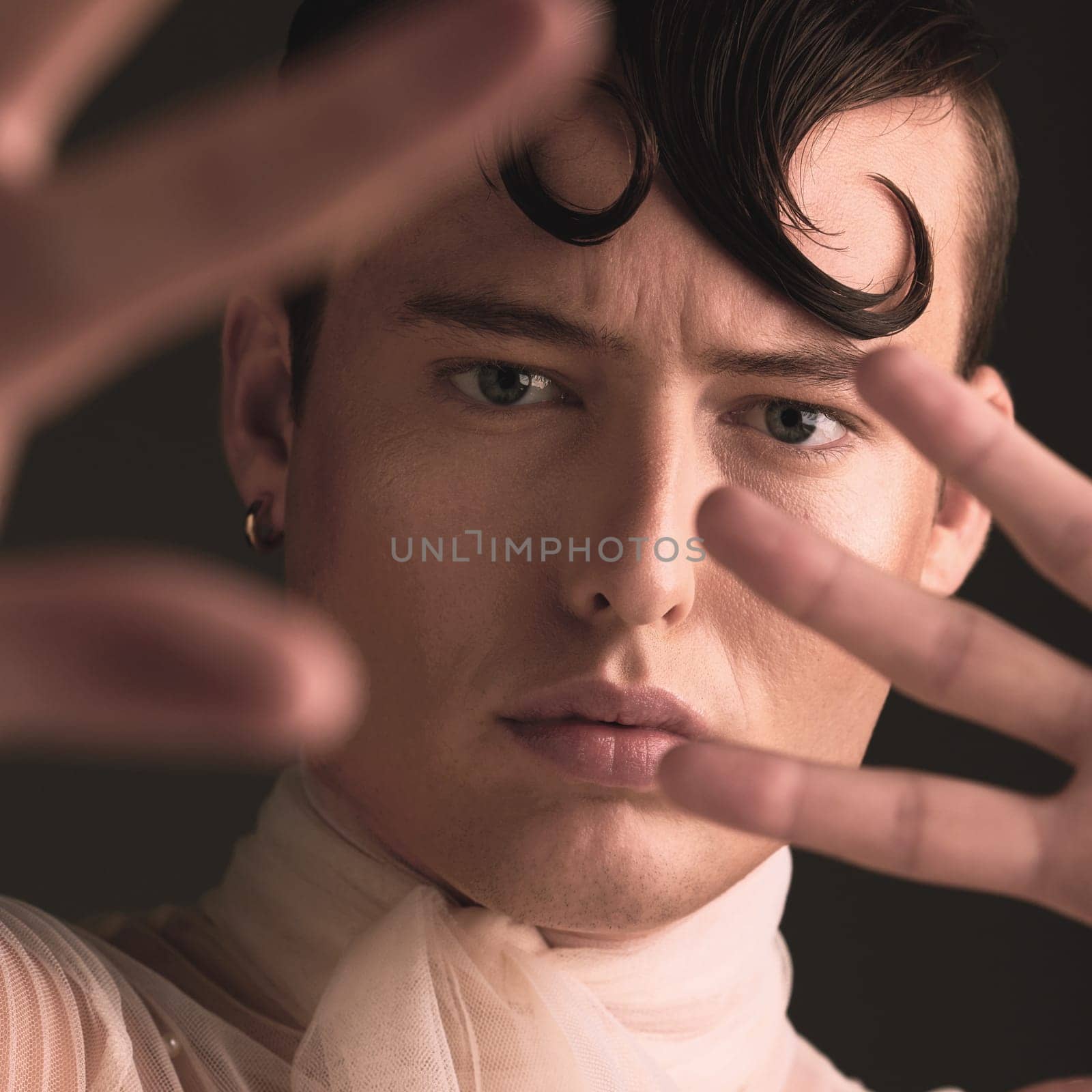 Beauty portrait of transgender man isolated on dark background for creative and queer fashion aesthetic. Young lgbtq model or gay person face with cosmetics, makeup and hands for art style in studio.