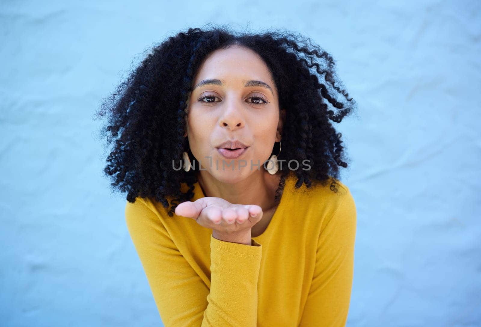 Black woman, portrait and blowing kiss for love, care and flirting on blue background, wall backdrop or outdoor. Young girl, hand kisses and expression of happiness, romance and kissing face emoji.