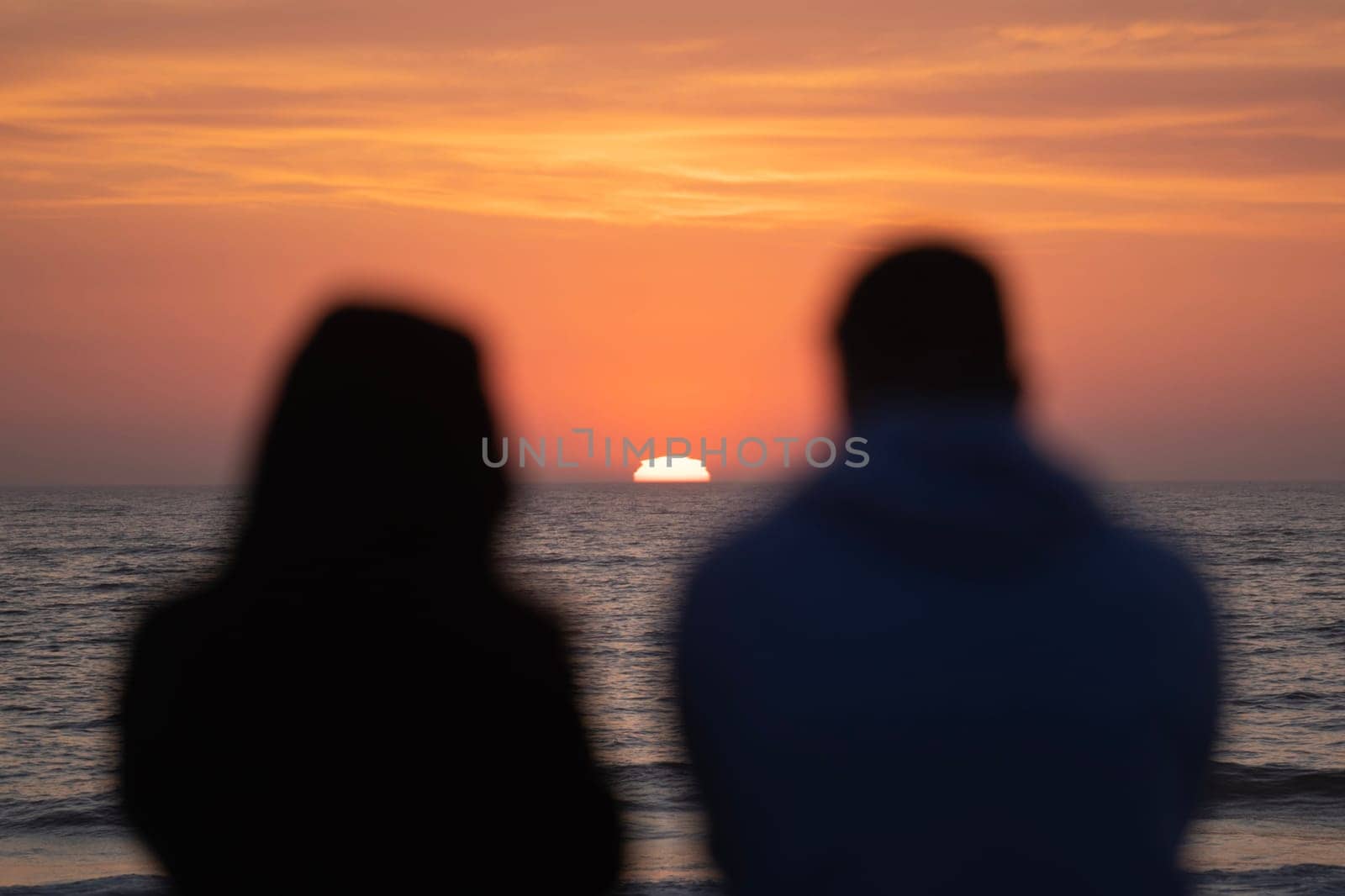 Blurred Silhouettes of boyfriend and girlfriend spending time on beach near waving sea against sundown sky in Furandoiro, Portugal