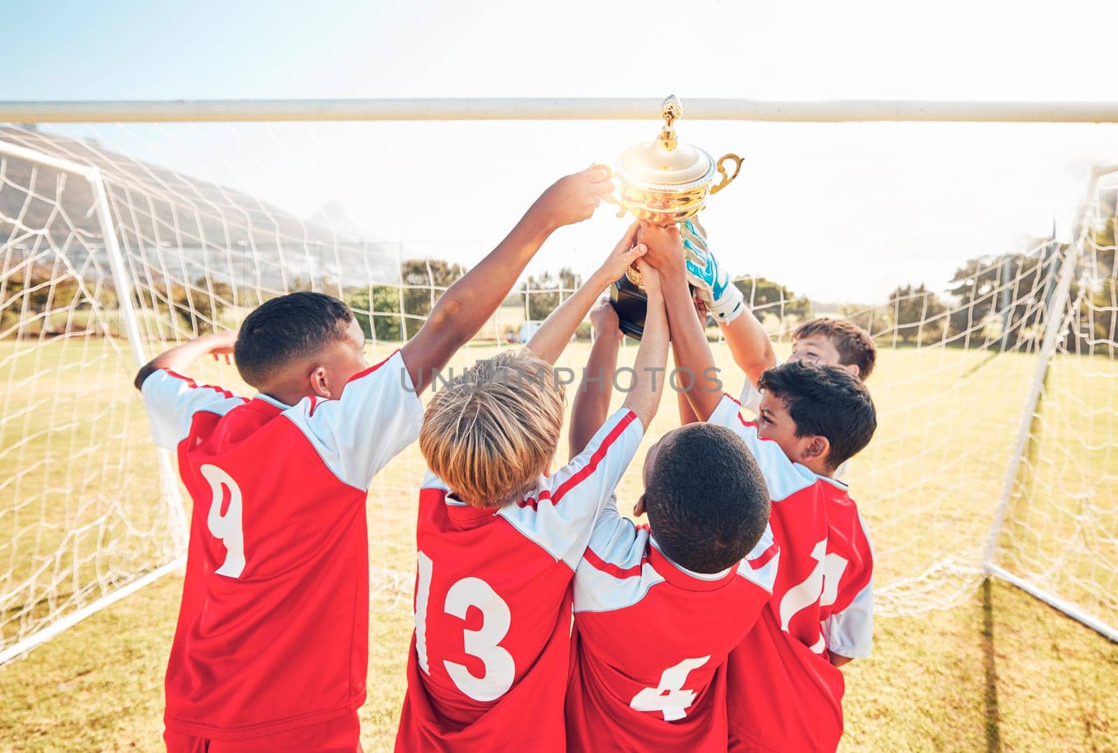 Children, winner and team soccer with trophy celebrating victory, achievement or match on the field. Kids in celebration for teamwork, sports and football match or game win together in the outdoors by YuriArcurs