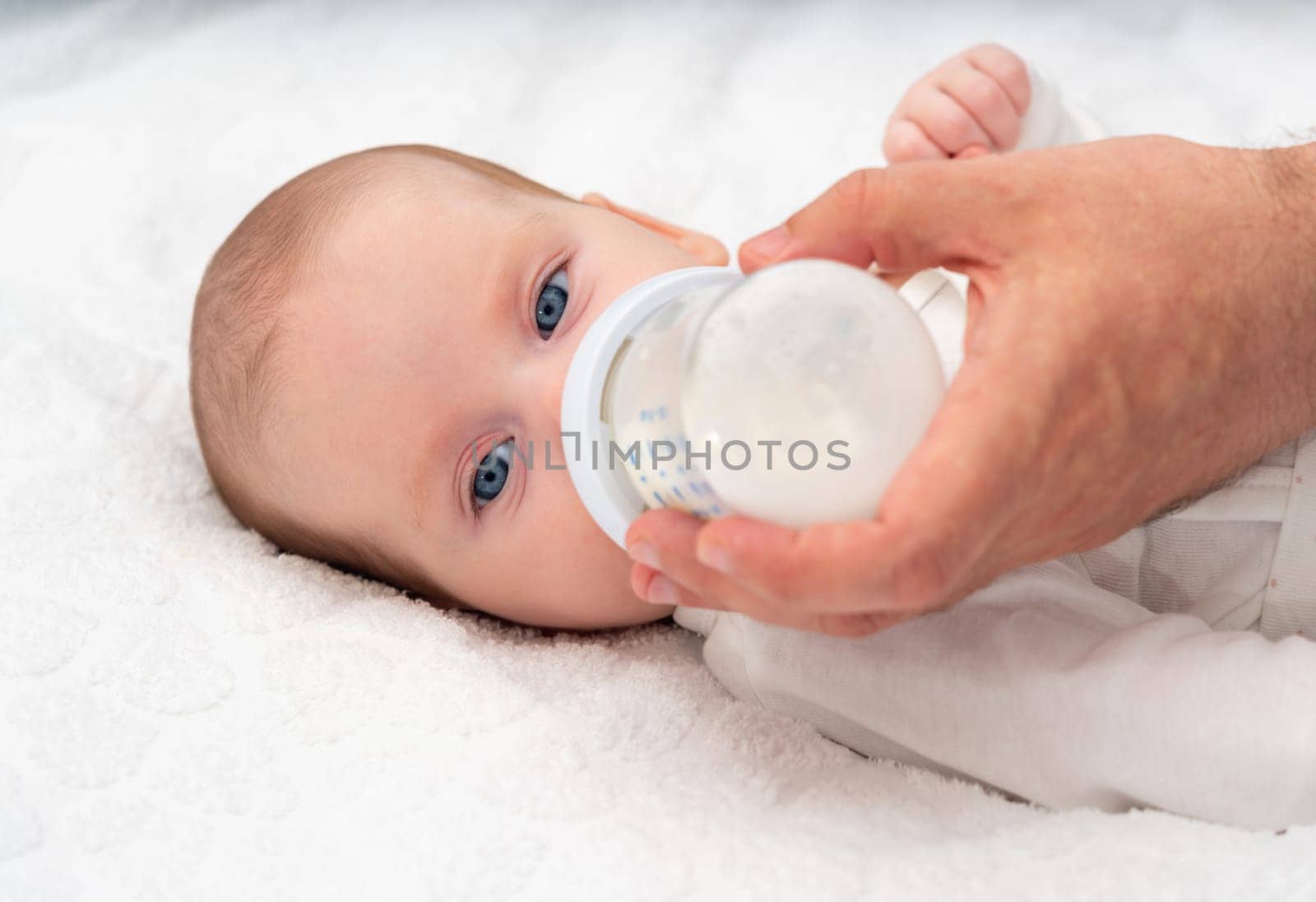Beautiful baby eats formula from a bottle supported by his father.