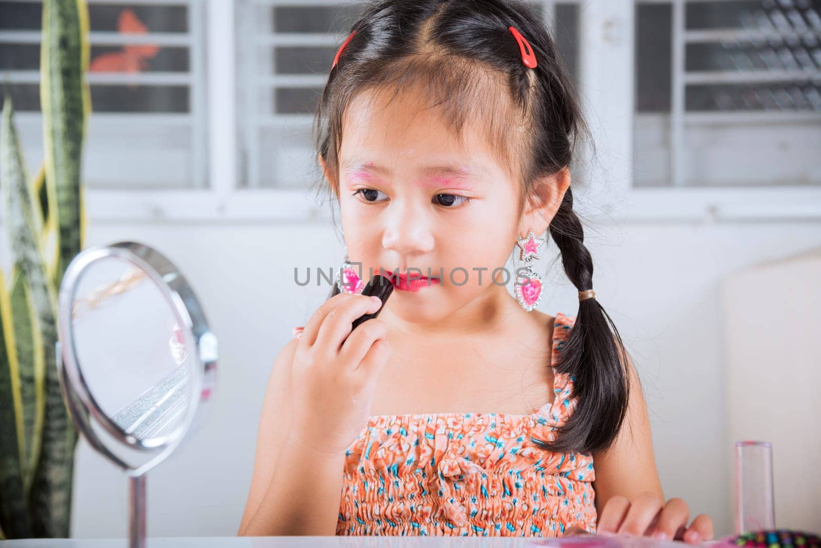 Happy kid is beautiful make up with cosmetics toy, Asian adorable funny little girl making makeup her face she looking in the mirror and applying red lipstick to mouth, Learning activity to be woman