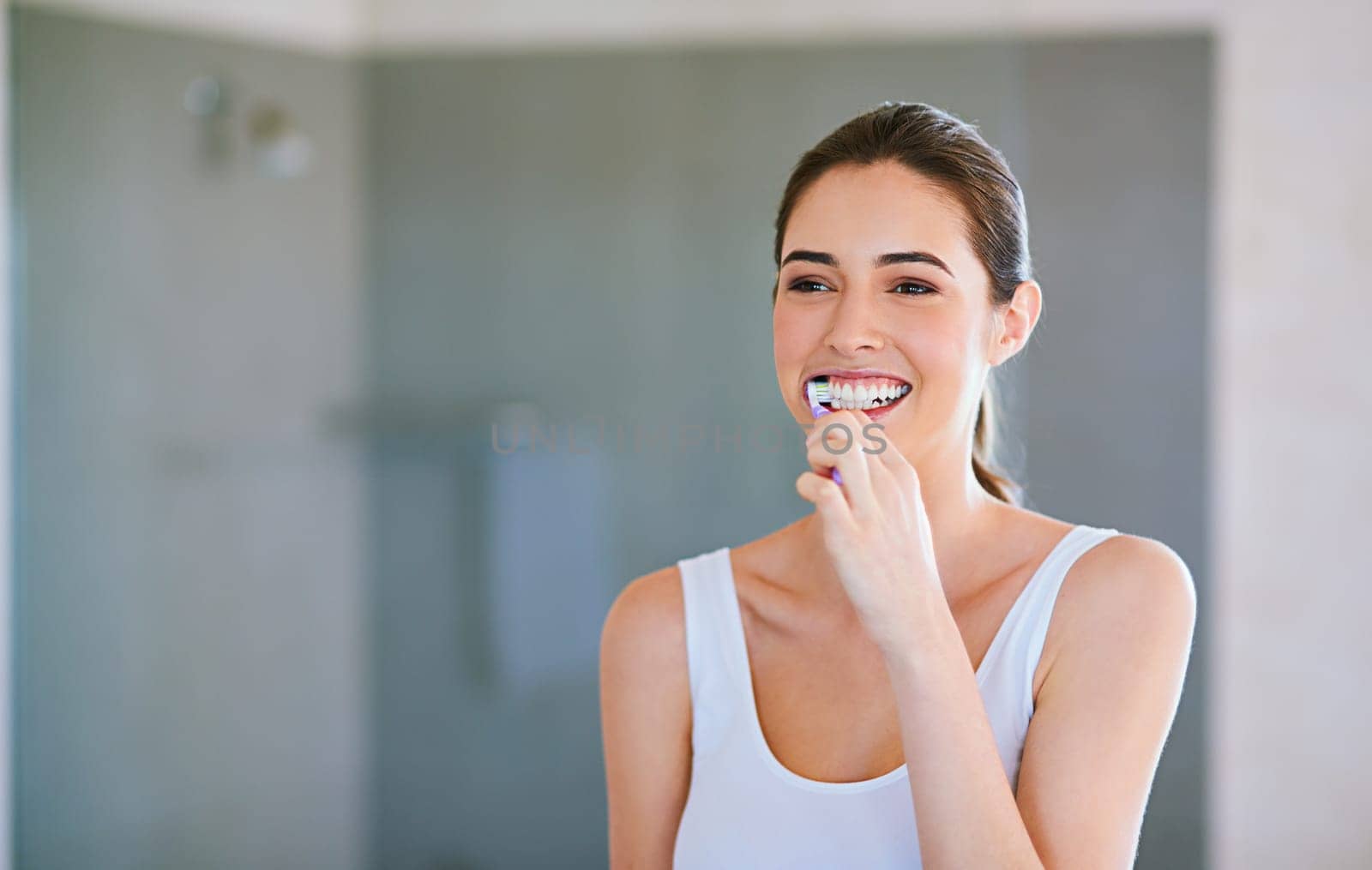 Toothbrush, toothpaste and woman brushing teeth in bathroom for health, happiness and wellness in morning. Girl, cleaning mouth for dental care and oral hygiene or smile in home with mockup space by YuriArcurs