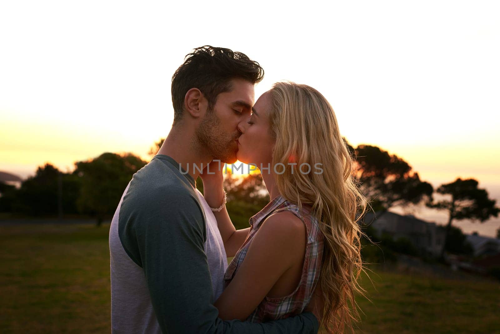 Couple kissing, nature and trees in sunset with love, romance and date on adventure, travel or honeymoon. Man, woman and kiss with hug, care and outdoor for safari, travel or travel in countryside.