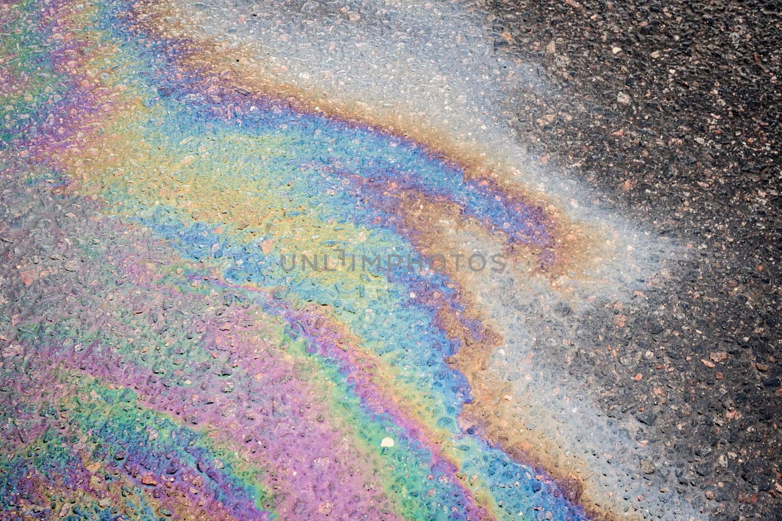 Oil stains from leaks in the car engine. Oil after rain makes spots with rainbow reflections refractive sun spectrum. Beautiful color mosaic, abstraction, ecology