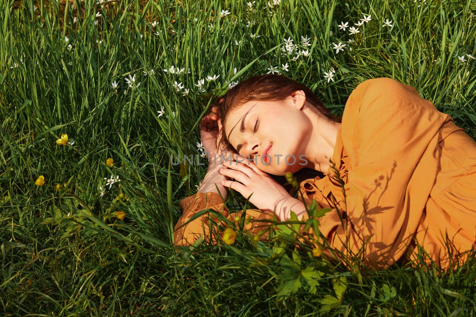 a close horizontal photo of a happy woman lying in the grass with her eyes closed and a pleasant smile on her face by Vichizh