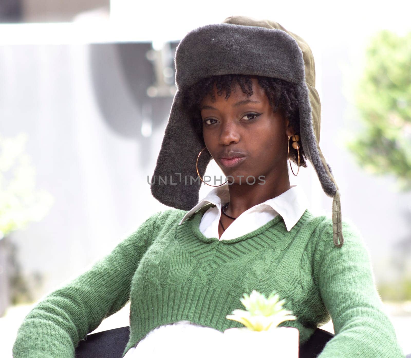 african american girl in a military hat posing serious looking at camera sitting on a chair on the street. High quality photo