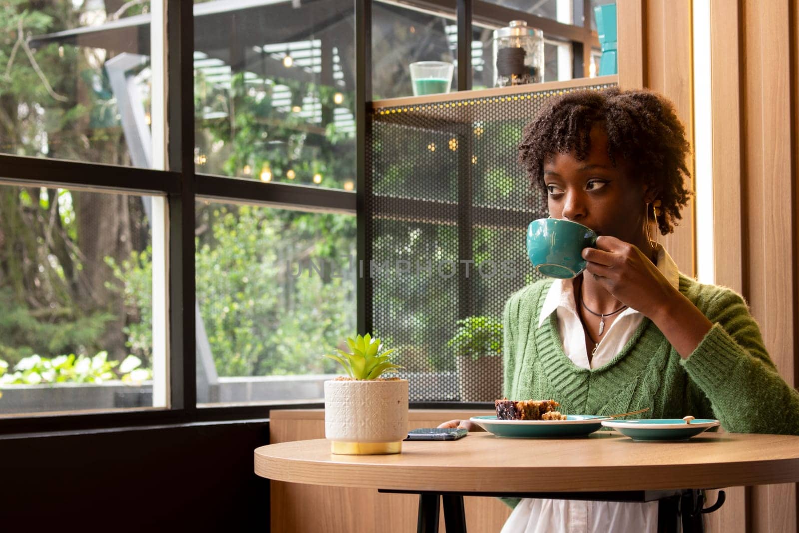 portrait and copy space of an african girl having a coffee happy and smiling looking at the street through a window. High quality photo