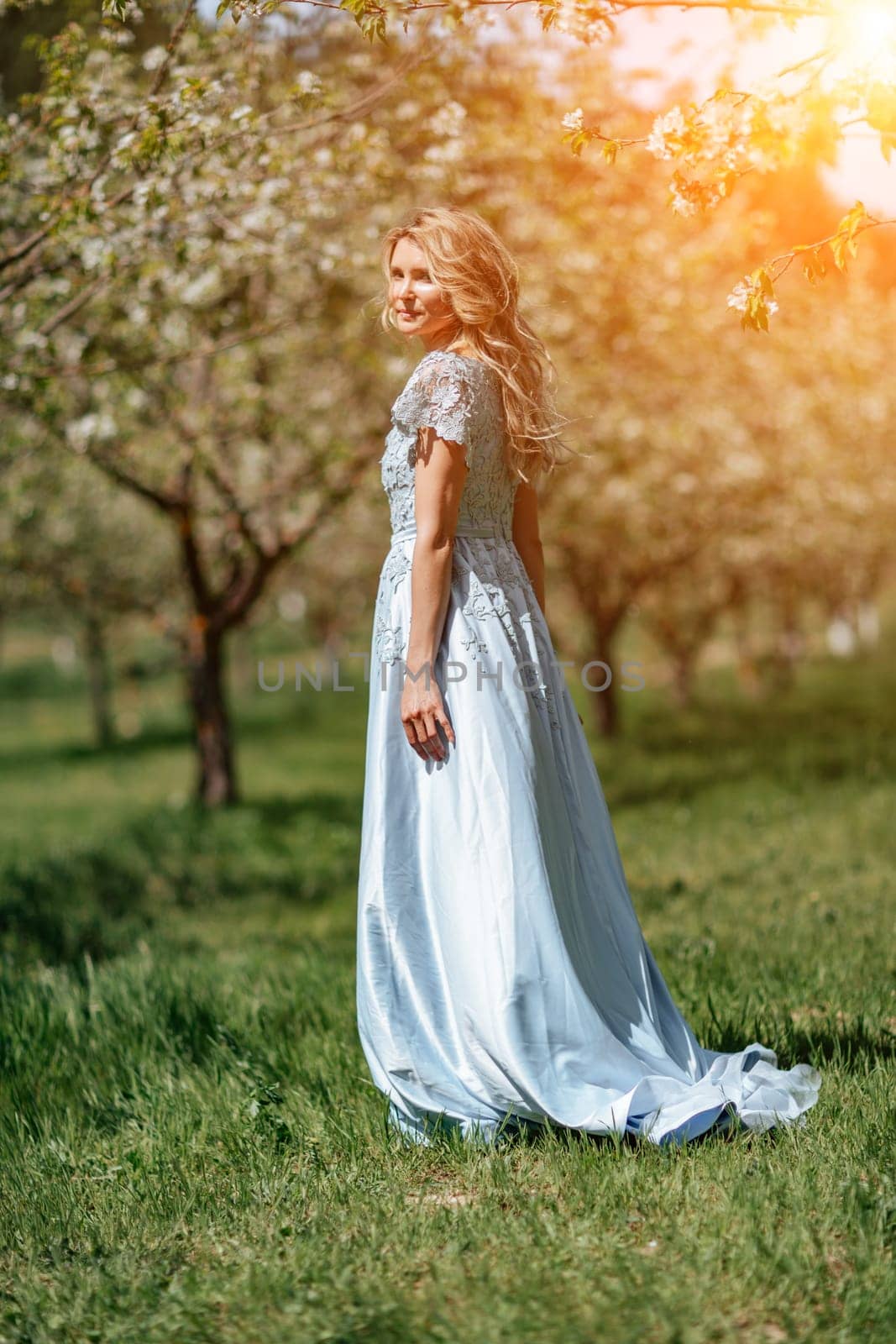 Blond garden. Portrait of a blonde in the park. Happy woman with long blond hair in a blue dress. by Matiunina