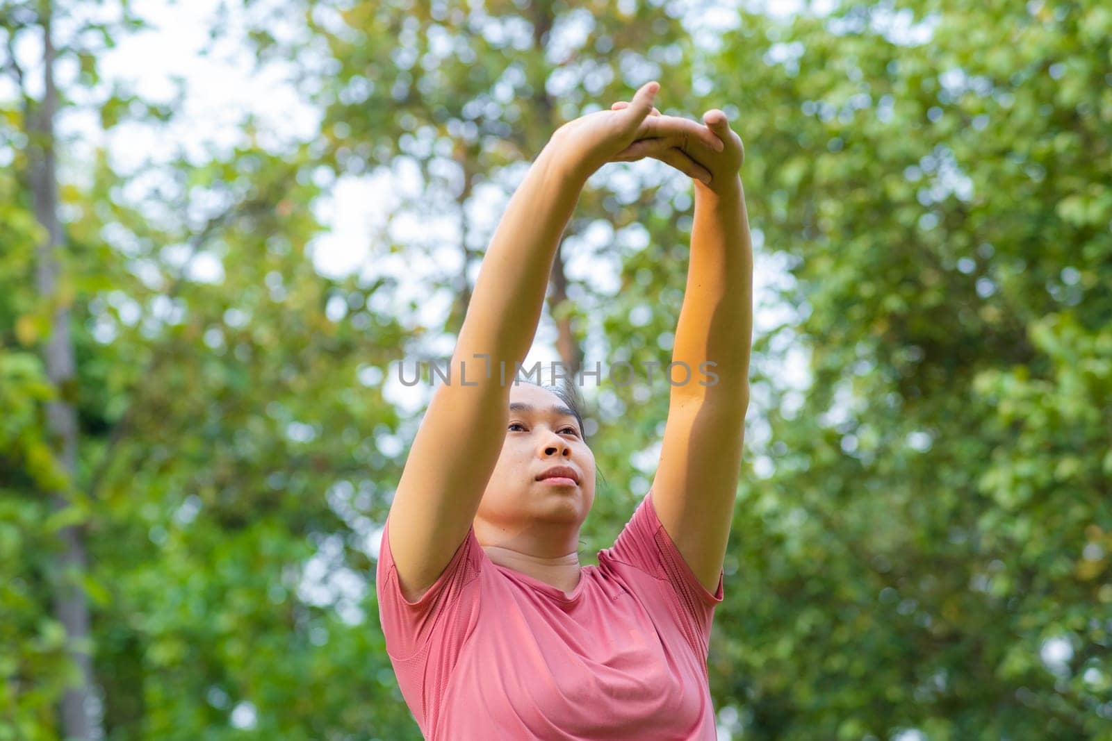 Young Asian woman in sportswear stretches before exercising in the park for a healthy lifestyle. Young healthy woman warming up outdoors. Healthy lifestyle concept. by TEERASAK