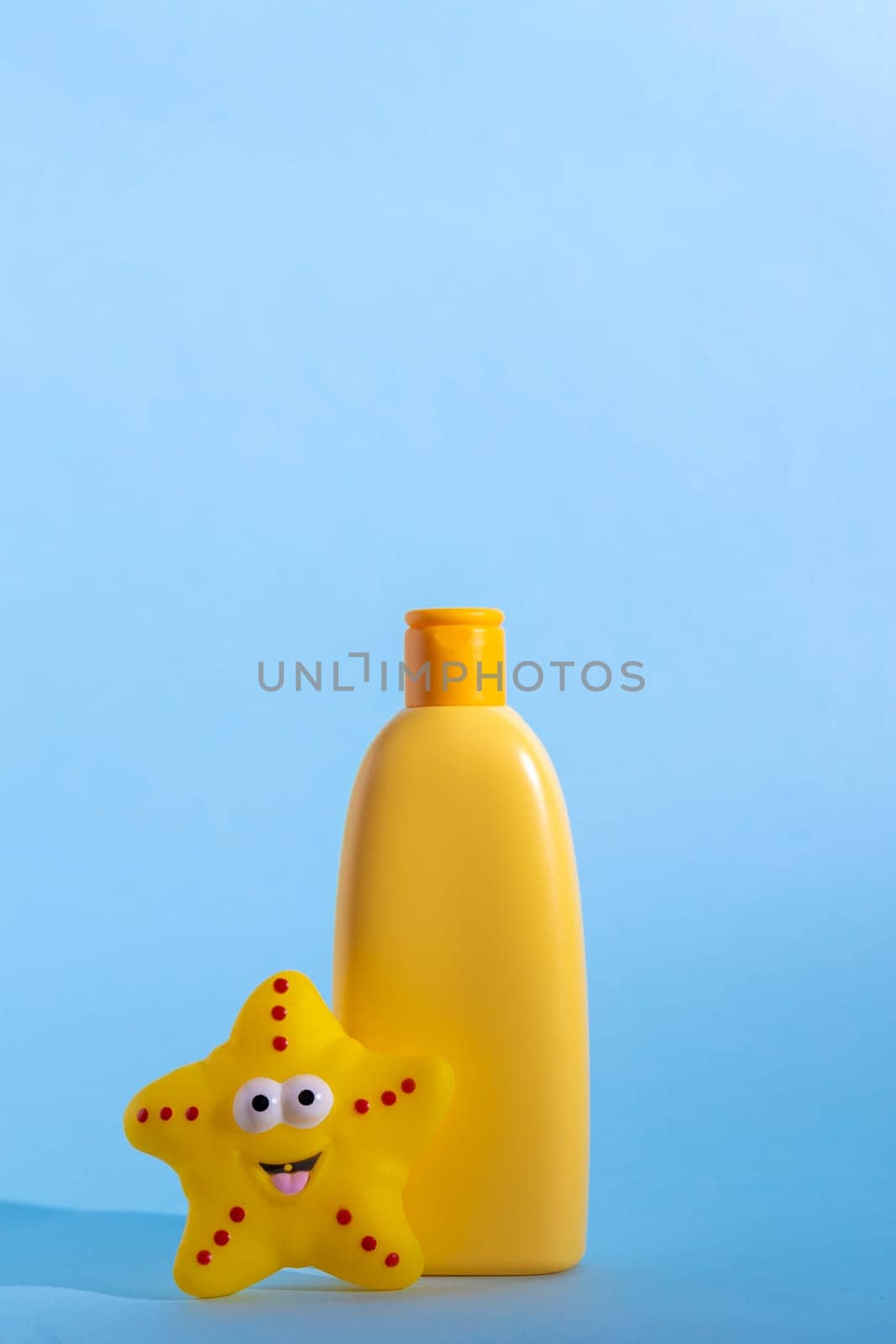 A yellow bottle with children's cosmetics with a place for a logo and funny toy on a light blue background. Copy space by Ri6ka
