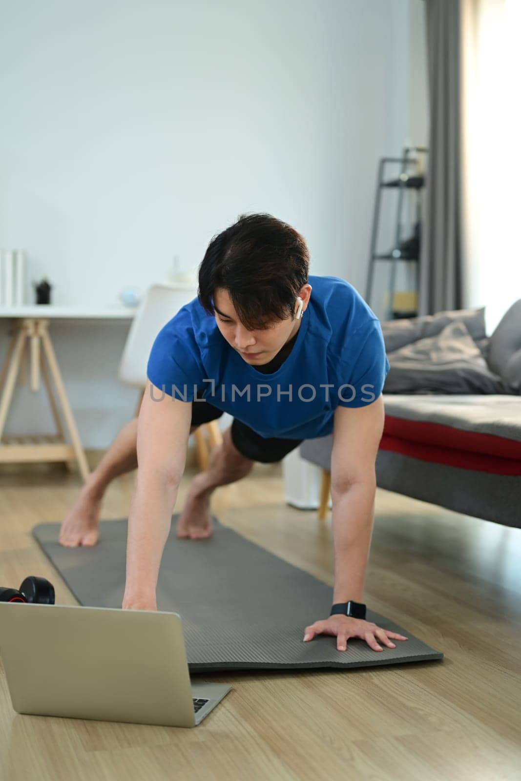 Muscular athletic man in sportswear working out at home and watching fitness lessons online on laptop.