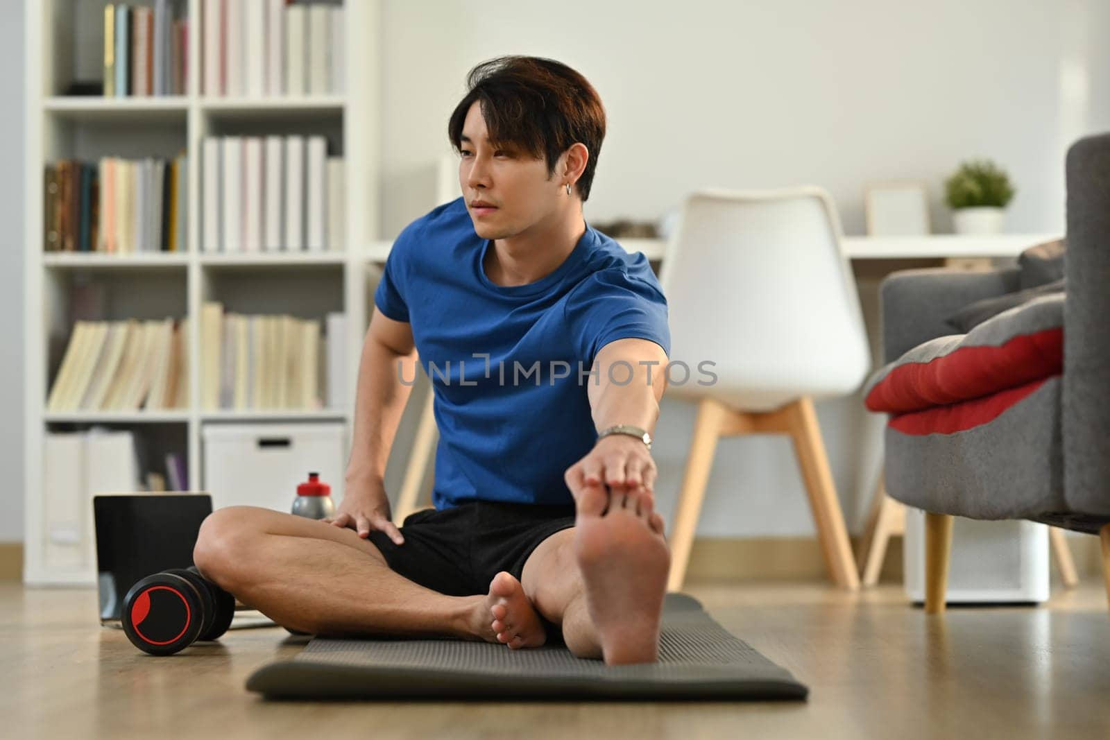 Active sportsman in fitness clothes stretching leg, preparing for morning workout at home. Healthy lifestyle concept.