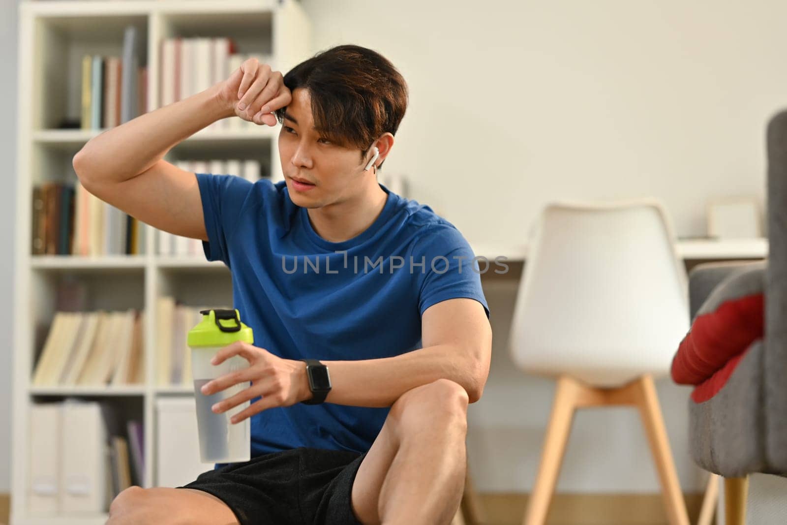 Male athlete holding a bottle of water, resting after his home workout and cardio exercises. Healthy lifestyle and fitness concept.