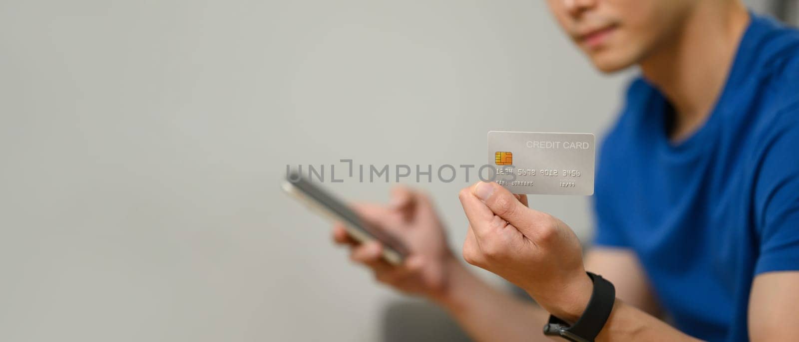 Man hand holding credit card and using smartphone for making online transactions or checking her bank account.
