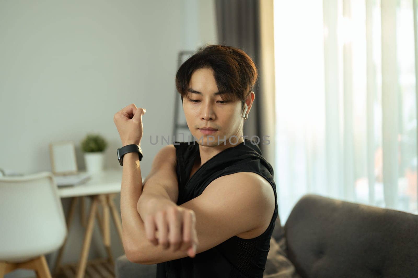 Asian man in sport outfit warming up in living room before workout. Healthy lifestyle and fitness concept.