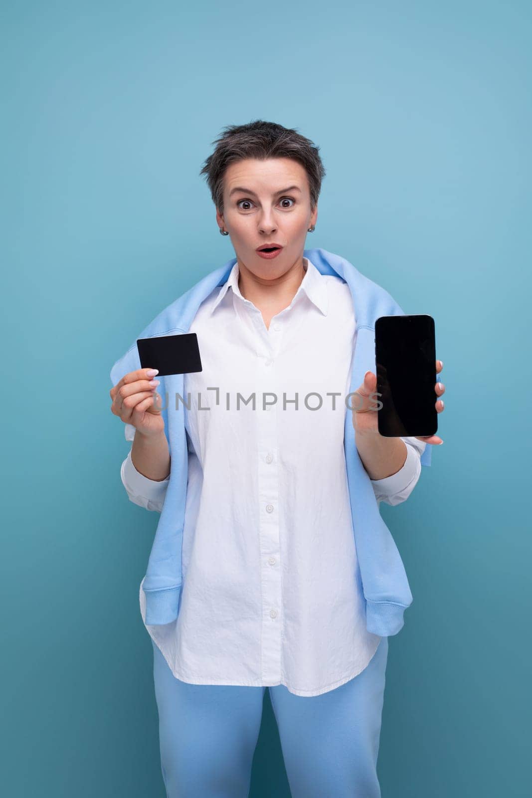 vertical photo of a stylish fashionable young lady with tousled hair in a white shirt with a credit card and a smartphone by TRMK