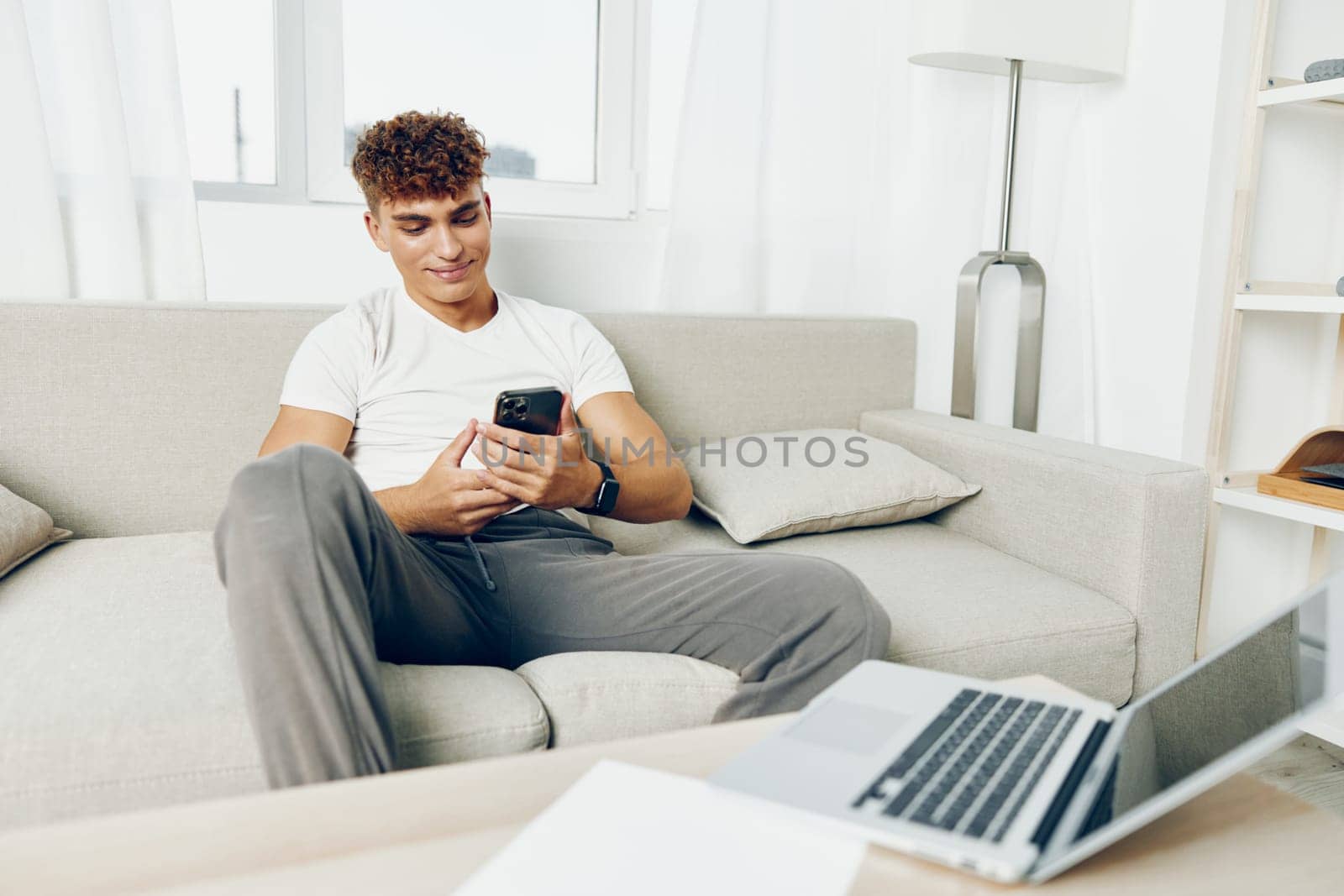 man interior phone couch adult smile laptop selfies communication sitting smartphone curly using smart holding cell home teenager modern