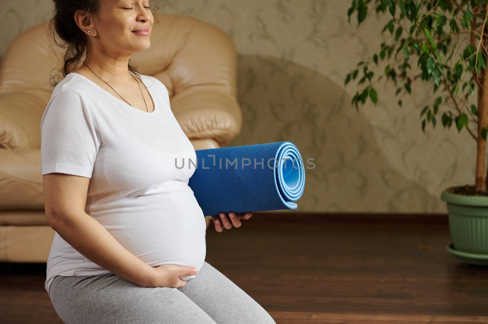 Delightful happy expectant pregnant woman, gravid female, future mother sitting in hero pose, touching her belly, enjoying active fitness lifestyle for healthy pregnancy. Yoga practice. Meditation