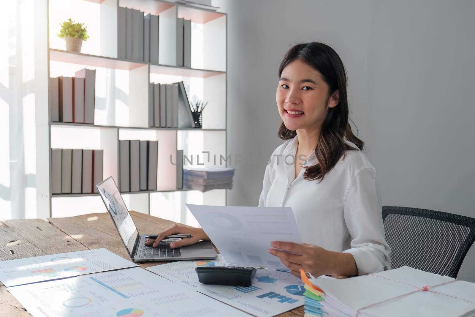 Asian businesswoman sit at their desks at office and calculate financial graphs showing results about their investments, plan a successful business growth process, diagrams on screen.