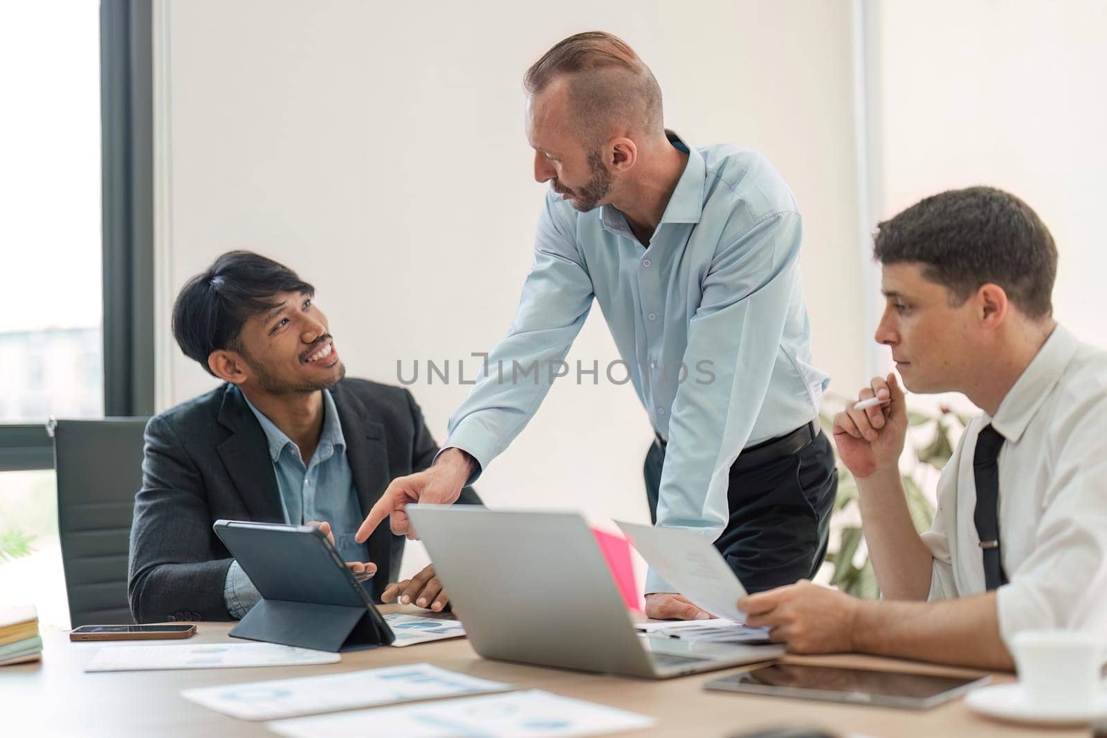 Business team discussing online project, showing computer presentation to skilled team leader. Friendly diverse colleagues working in pairs on laptop.