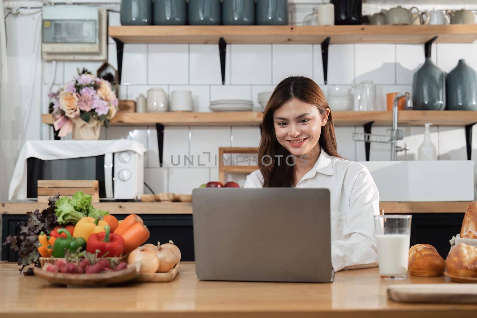 Asian young woman use laptop in the kitchen at home.