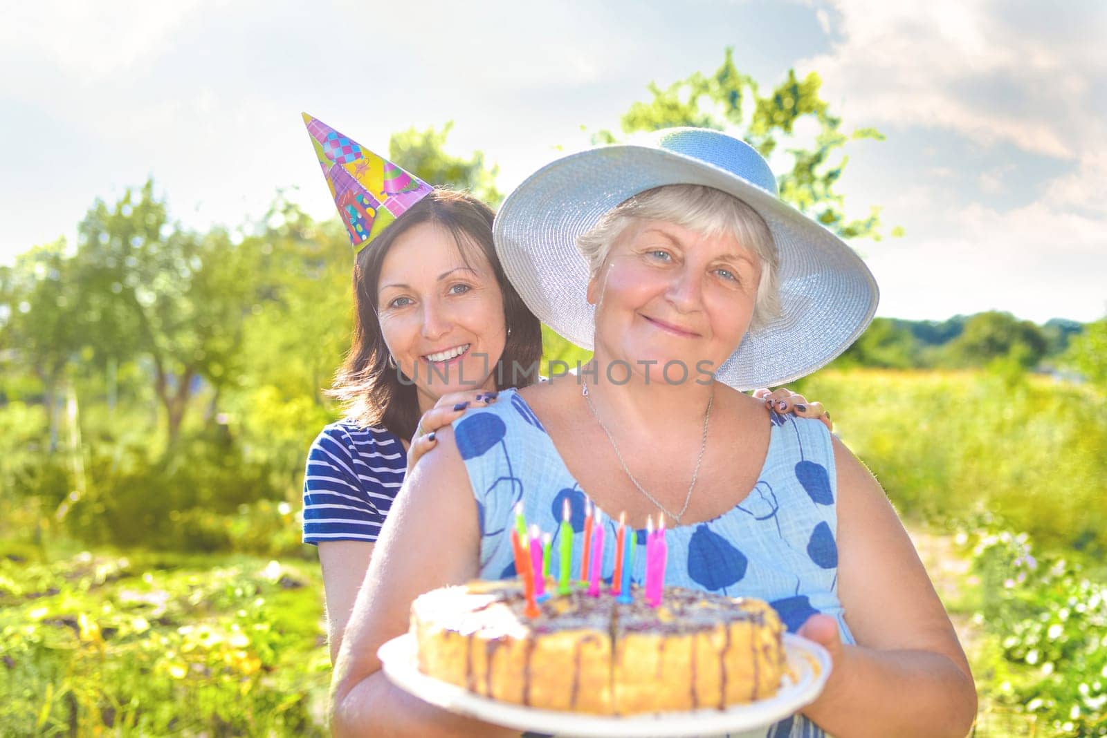 Grandmother's birthday, who with a smile, together with her daughter in the village and holds a birthday homemade cake. by Nickstock