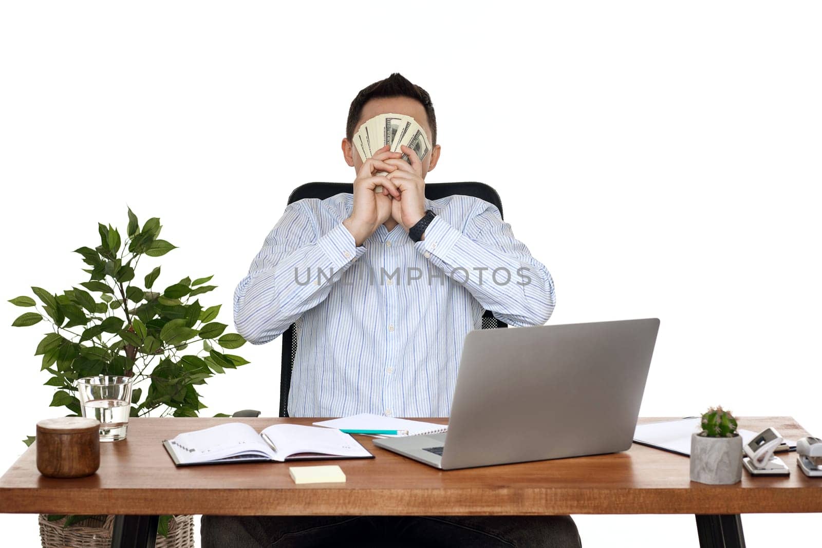 happy businessman using laptop and holding money while sitting on chair at desk.