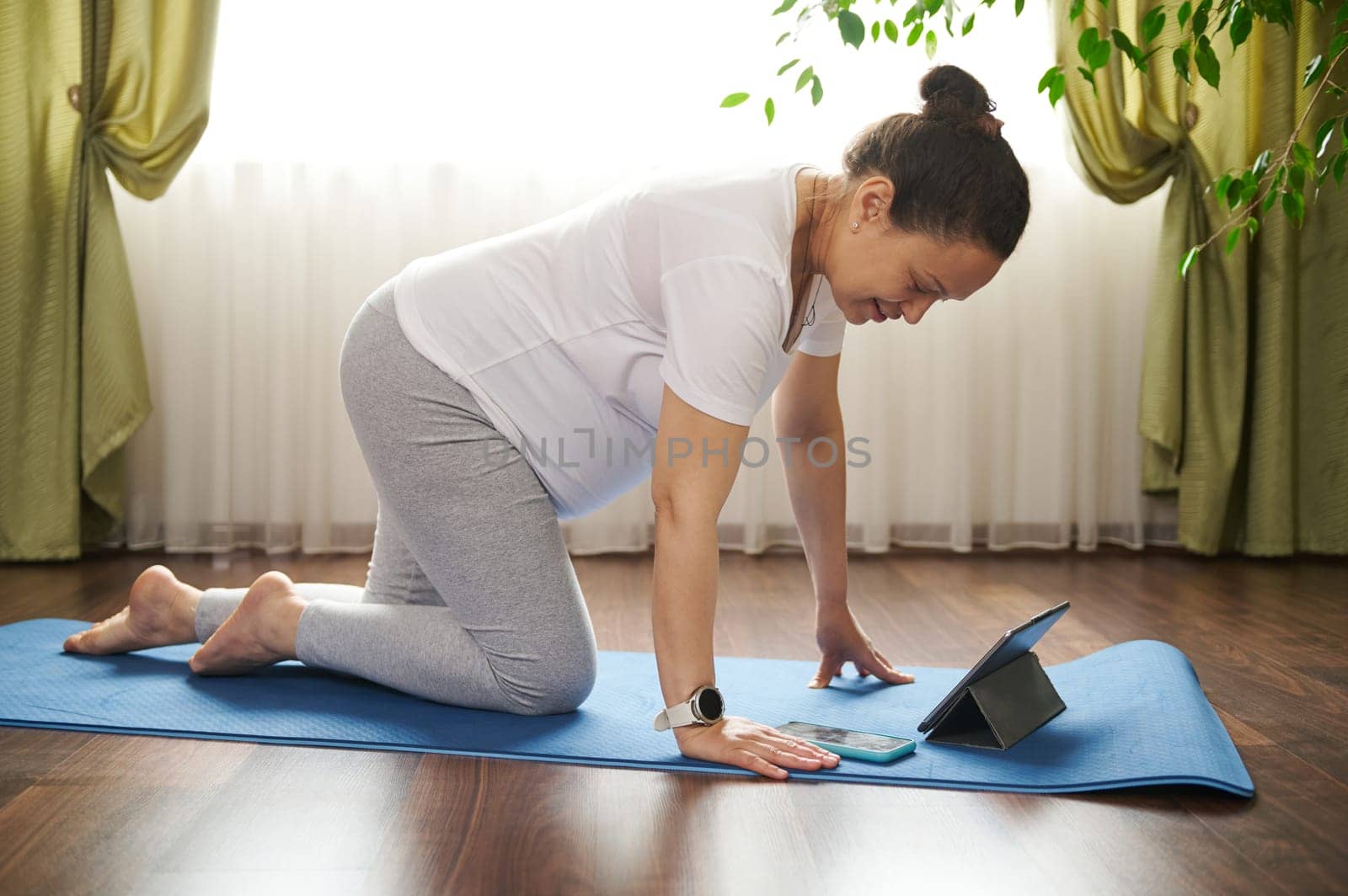 African American active pregnant woman using smartphone during online yoga practice, standing in table posture on a blue exercise mat. Pregnancy. Maternity. People. Sport. technology. Mobile app.