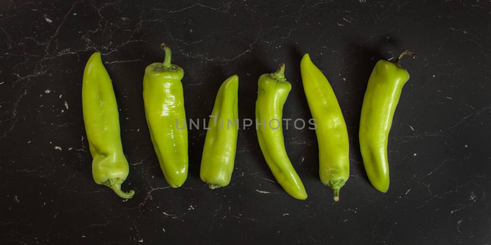 Top down view, green pointed peppers on black board.