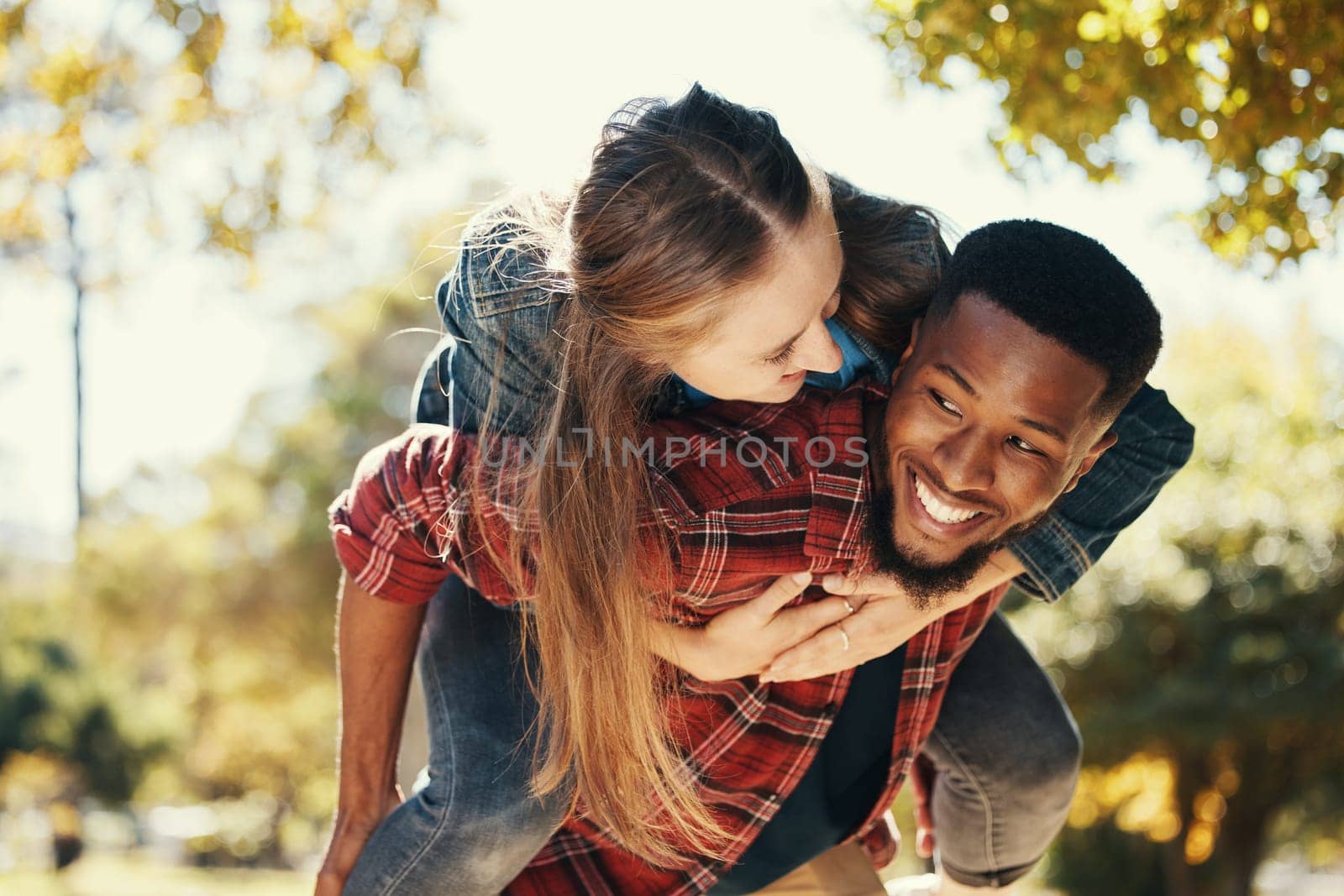 Piggy back, couple and love in park, smile and happy on date, romance and fun together in spring nature. Interracial man and woman happiness, play or relationship outdoor in forest, care or woods by YuriArcurs
