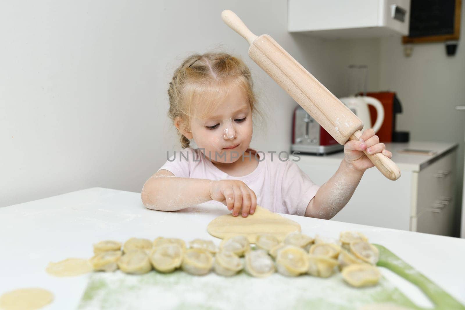 Little girl in flour prepares dumplings in the kitchen
