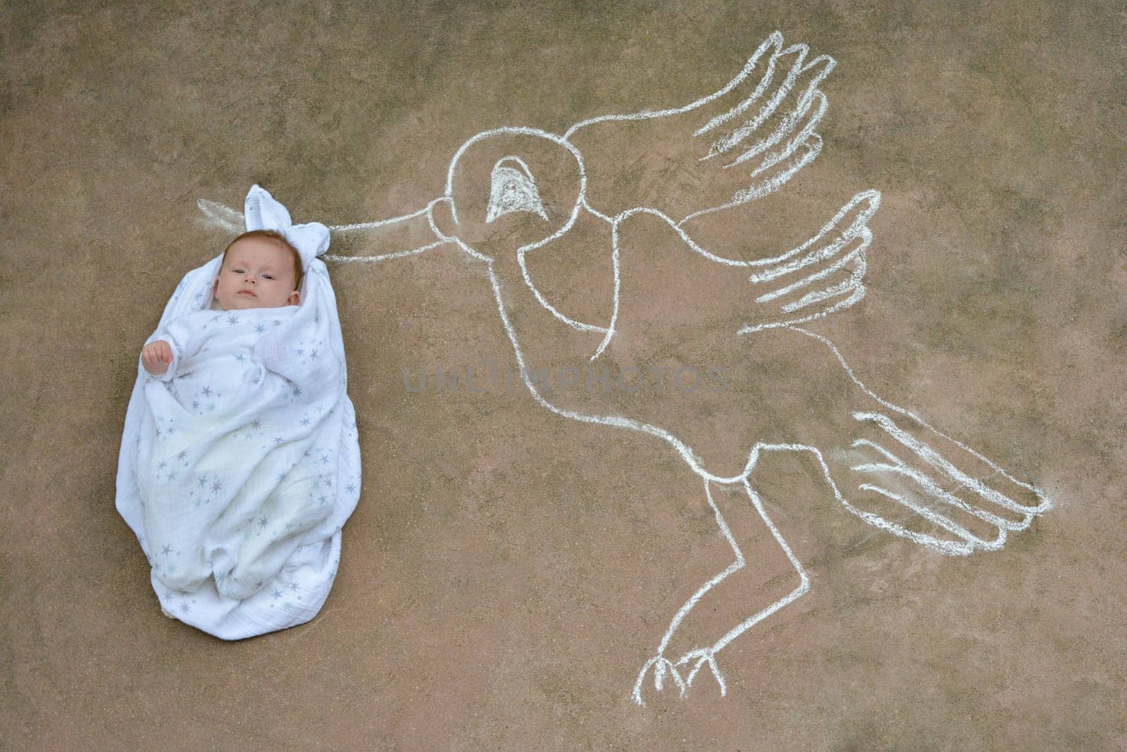 A stork holding a newborn baby in a white blanket