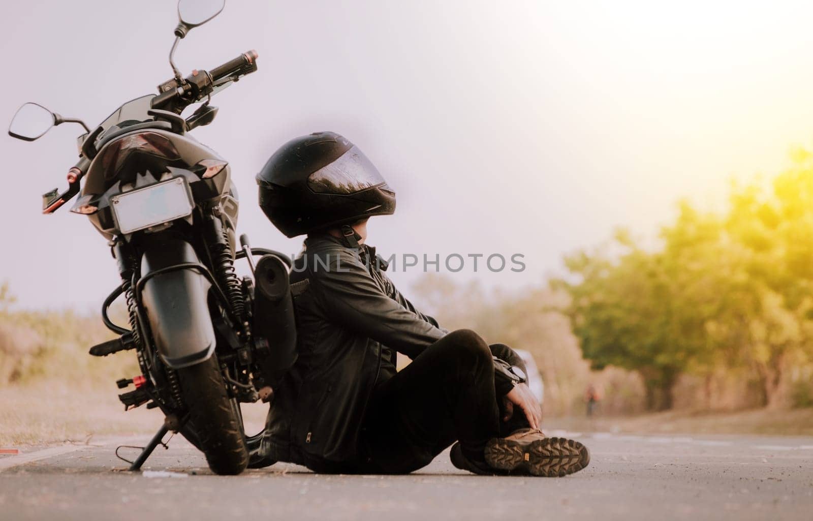 Motorcyclist sitting next to his motorcycle on the road. Motorcyclist sitting and leaning on his motorcycle on the asphalt by isaiphoto