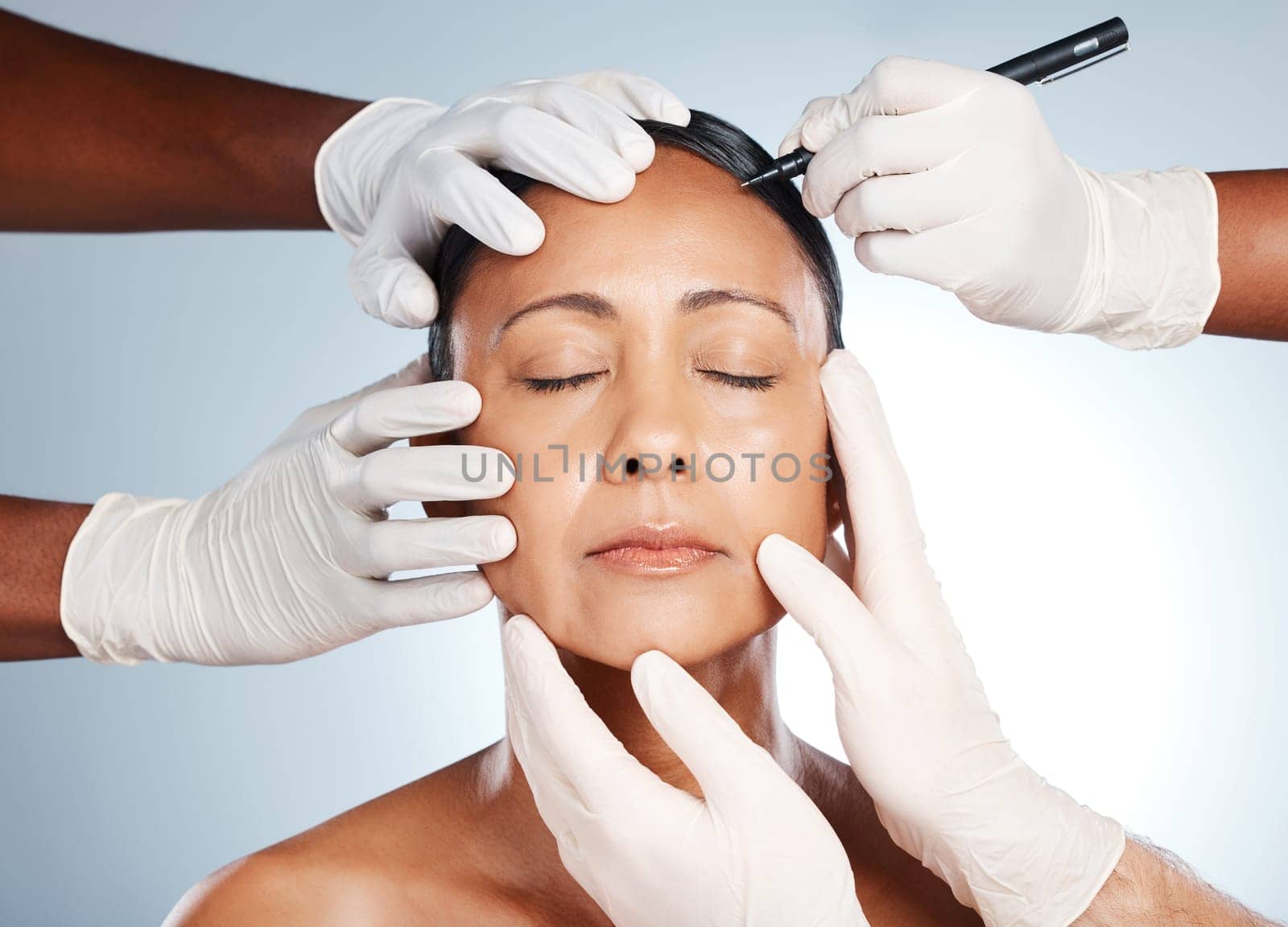 Woman, face and hands with pen for plastic surgery, beauty or cosmetic process by studio background with surgeon. Senior model, botox and collagen for antiaging, skincare and dermatology with doctor.