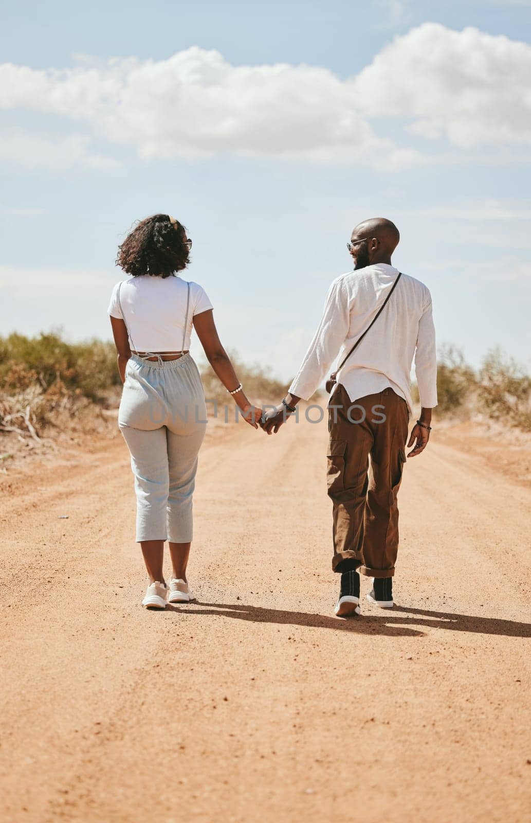 Black couple, love and holding hands back view in nature walking on vacation on desert, sand or dirt road. Romance, safari and man, woman and bonding, care or spending time together on outdoors date