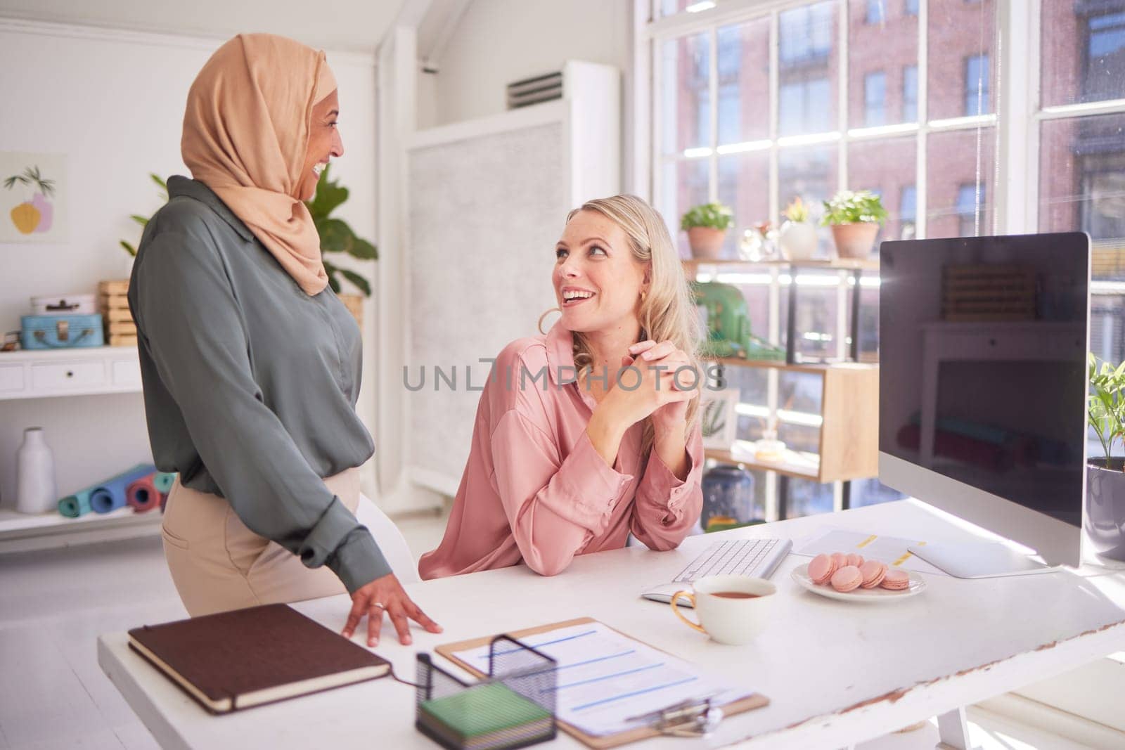 Business people, office and women talking at desk, chatting or discussion. Meeting, communication and happy manager in casual conversation with employee or colleague on break at company workplace