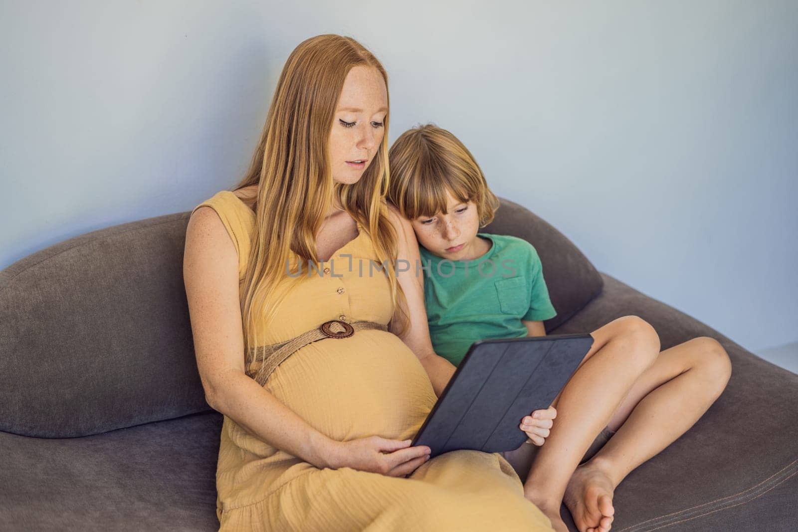 pregnant mom and son look at the tablet. Reading a book or watching a cartoon or making a video call. Look at the photo from the ultrasound.