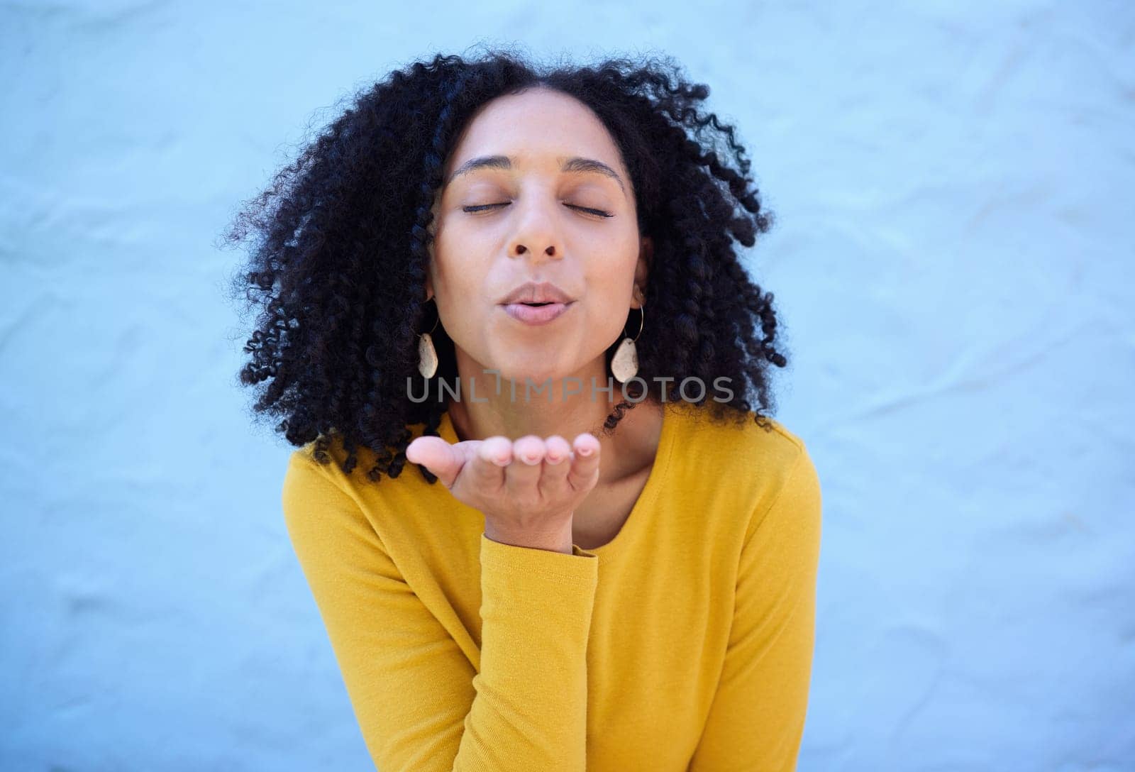 Black woman blowing kiss in air for love, care and flirting on blue background, wall backdrop or outdoor. Young girl, hand kisses and expression of happiness, romance and kissing face emoji with lips.