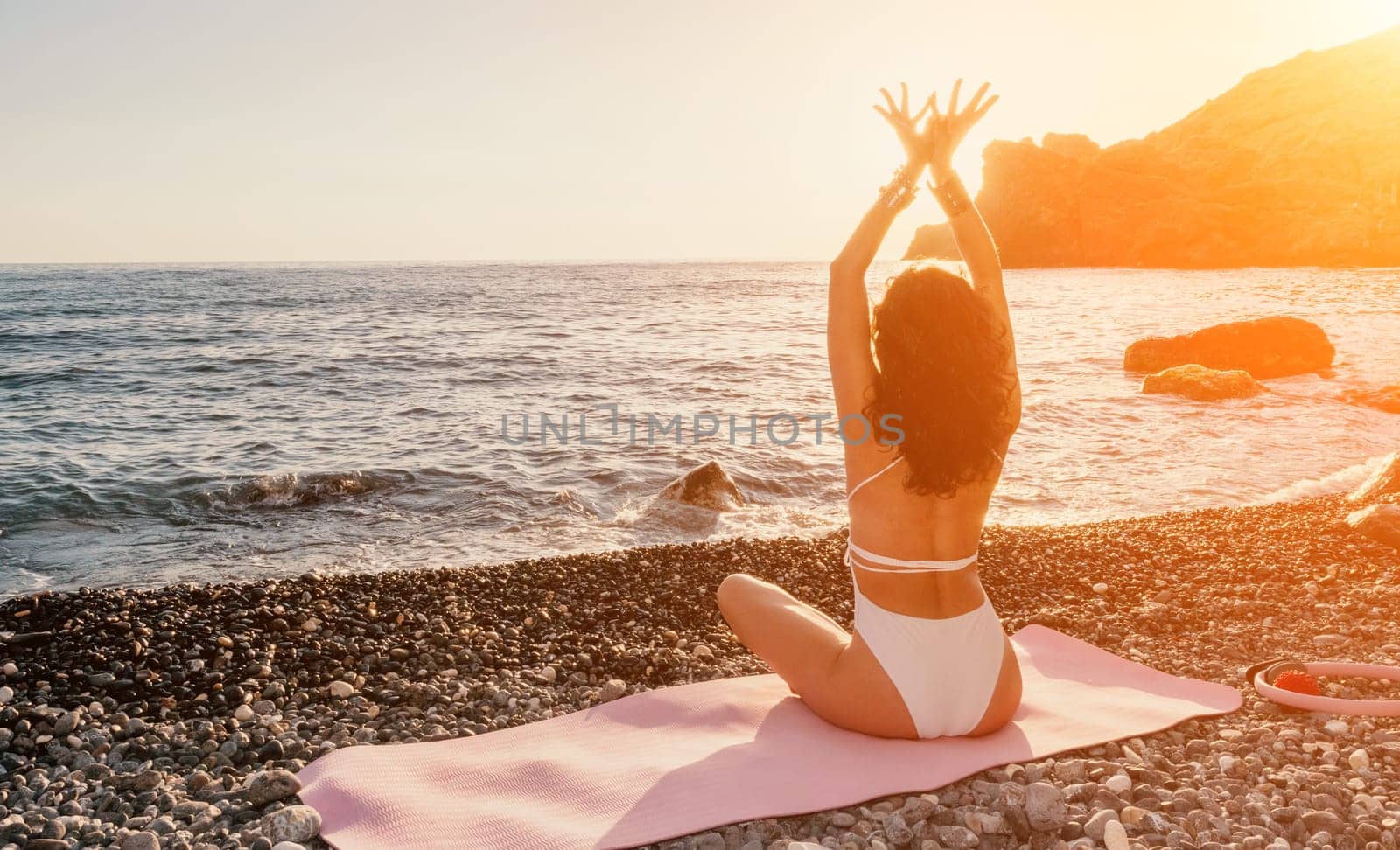 Young woman in swimsuit with long hair practicing stretching outdoors on yoga mat by the sea on a sunny day. Women's yoga fitness pilates routine. Healthy lifestyle, harmony and meditation concept.