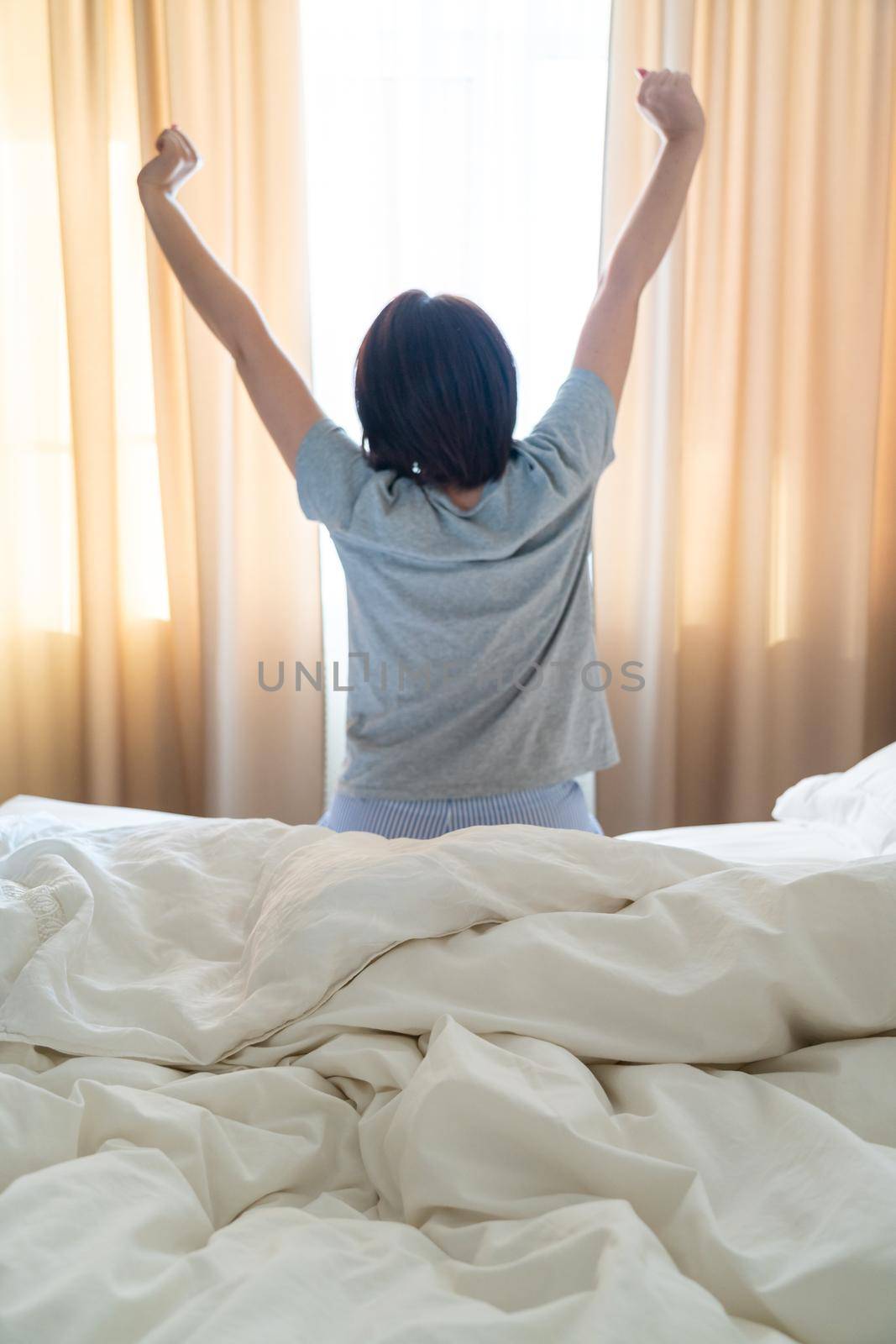 Woman stretching in bed after wake up, back view by Mariakray