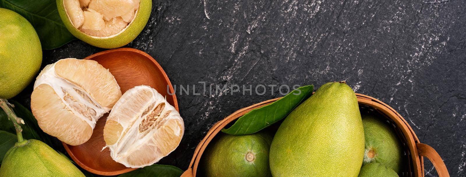 Fresh pomelo, grapefruit in bamboo basket with green leaf on dark black slate background. Seasonal fruit for Mid-Autumn Festival. Top view. Flat lay.