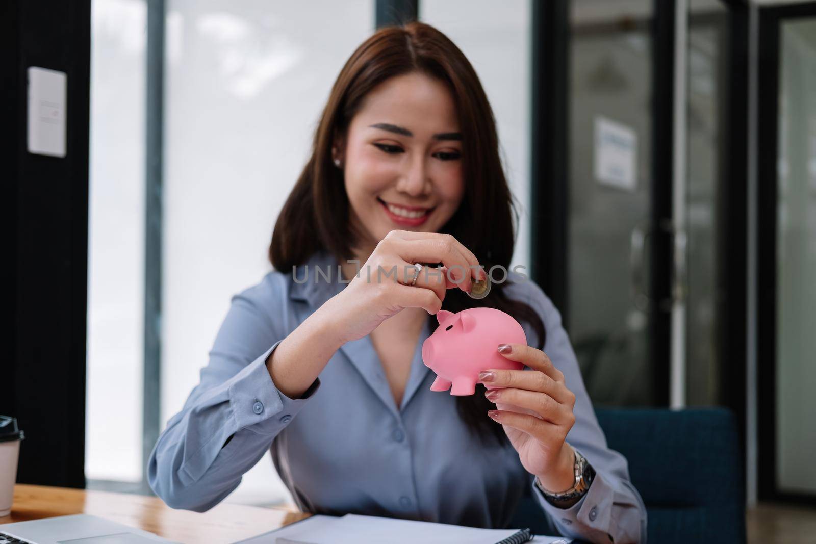 Close up hand of beauty asian woman putting money coin into pink piggy bank for saving money wealth and financial concept.