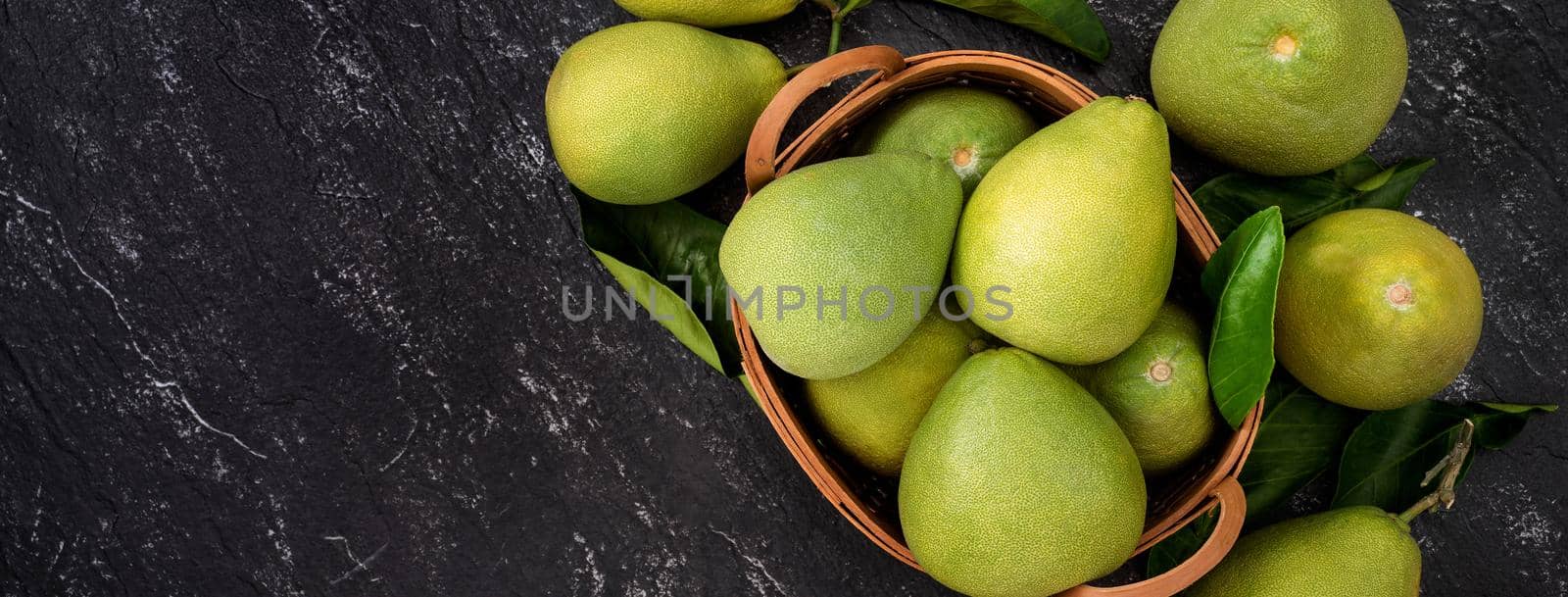 Fresh pomelo, grapefruit in bamboo basket with green leaf on dark black slate background. Seasonal fruit for Mid-Autumn Festival. Top view. Flat lay.