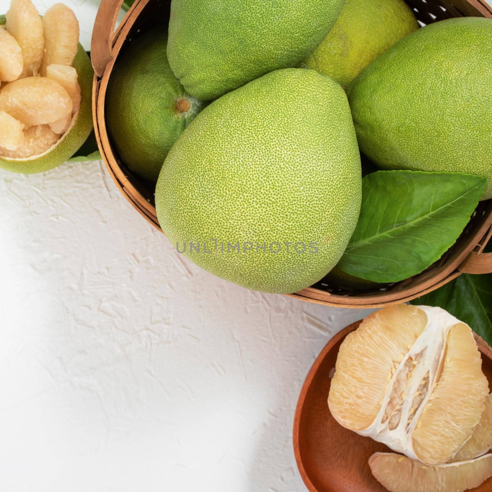 Fresh pomelo, grapefruit in bamboo basket with green leaf on bright white background. Seasonal fruit for Mid-Autumn Festival. Top view. Flat lay.