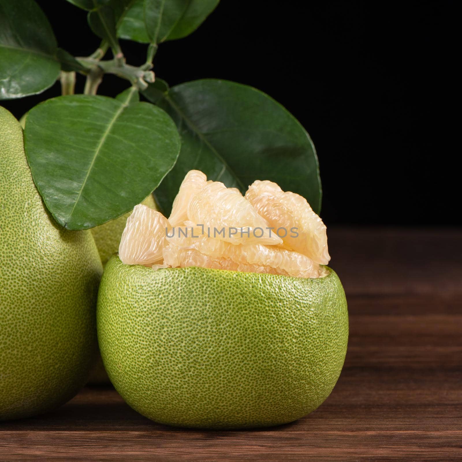 Fresh peeled pomelo, grapefruit, shaddock with green leaves on dark wooden plank table. Seasonal fruit near mid-autumn festival, close up, copy space