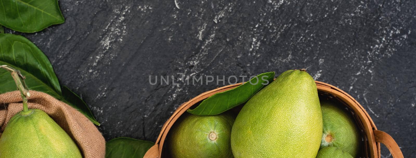 Fresh pomelo, pummelo, grapefruit, shaddock in bamboo basket with leaf on dark black slate background. Seasonal fruit concept. Top view. Flat lay. by ROMIXIMAGE