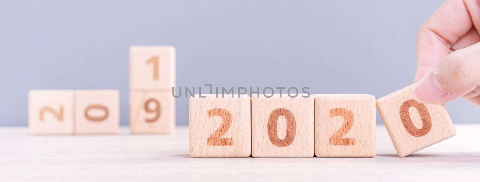 Abstract 2020 & 2019 New year countdown design concept - woman holding wood blocks cubes on wooden table and blue background, close up, copy space. by ROMIXIMAGE