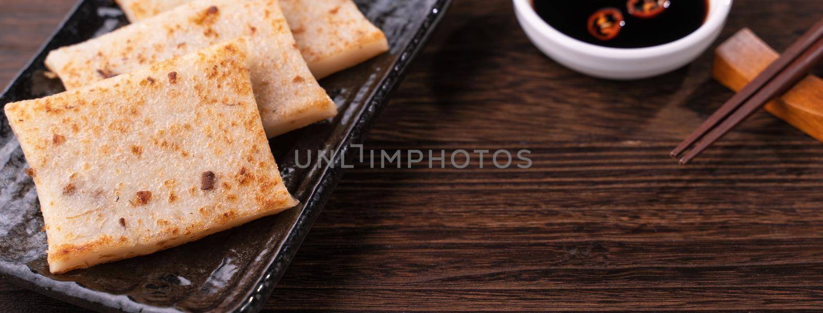 Delicious turnip cake, Chinese traditional local dish radish cake in restaurant with soy sauce and chopsticks, close up, copy space. by ROMIXIMAGE