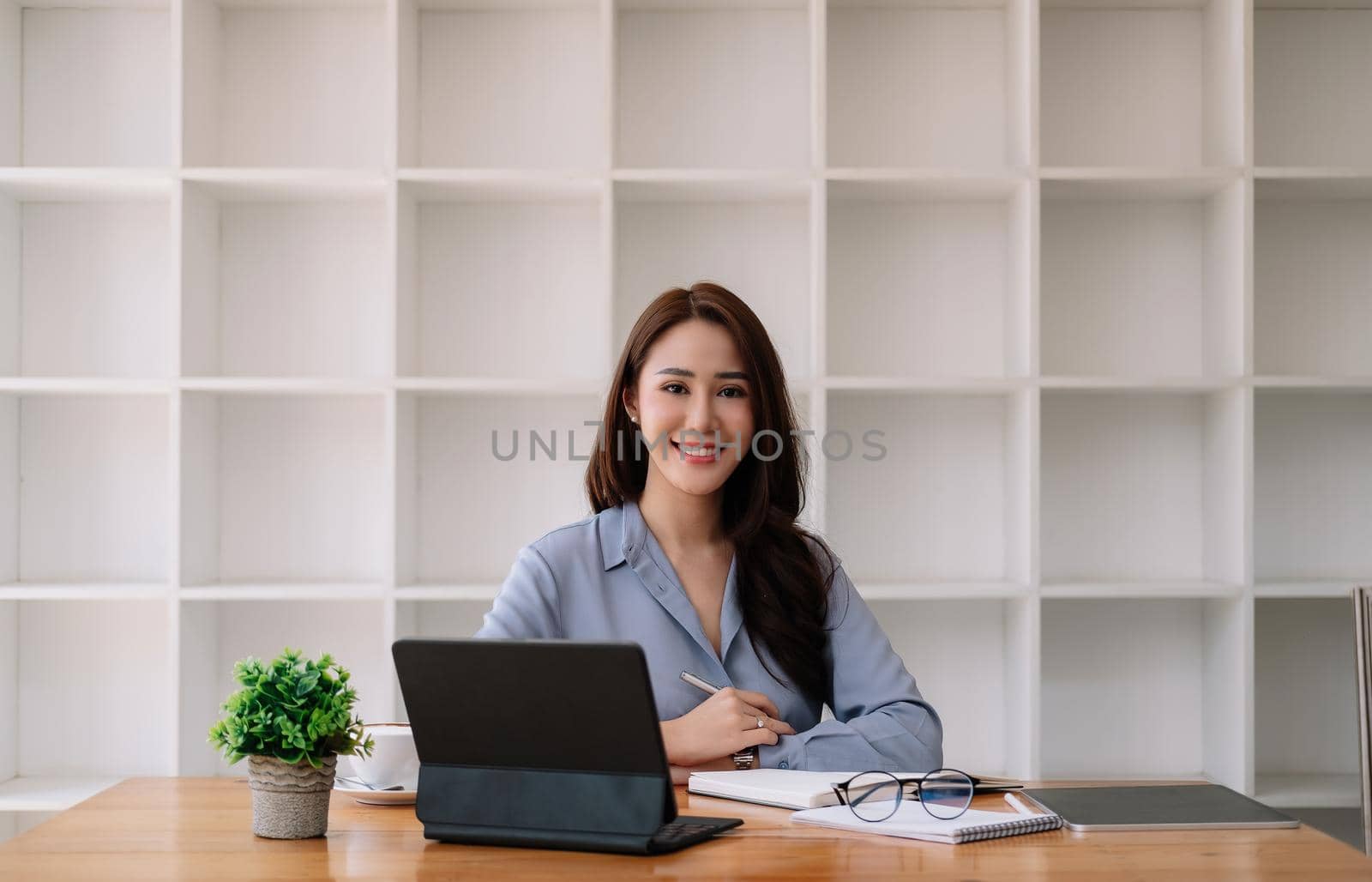 Portrait Attractive Asian Businesswoman working with smart tablet on wooden desk at her office by nateemee